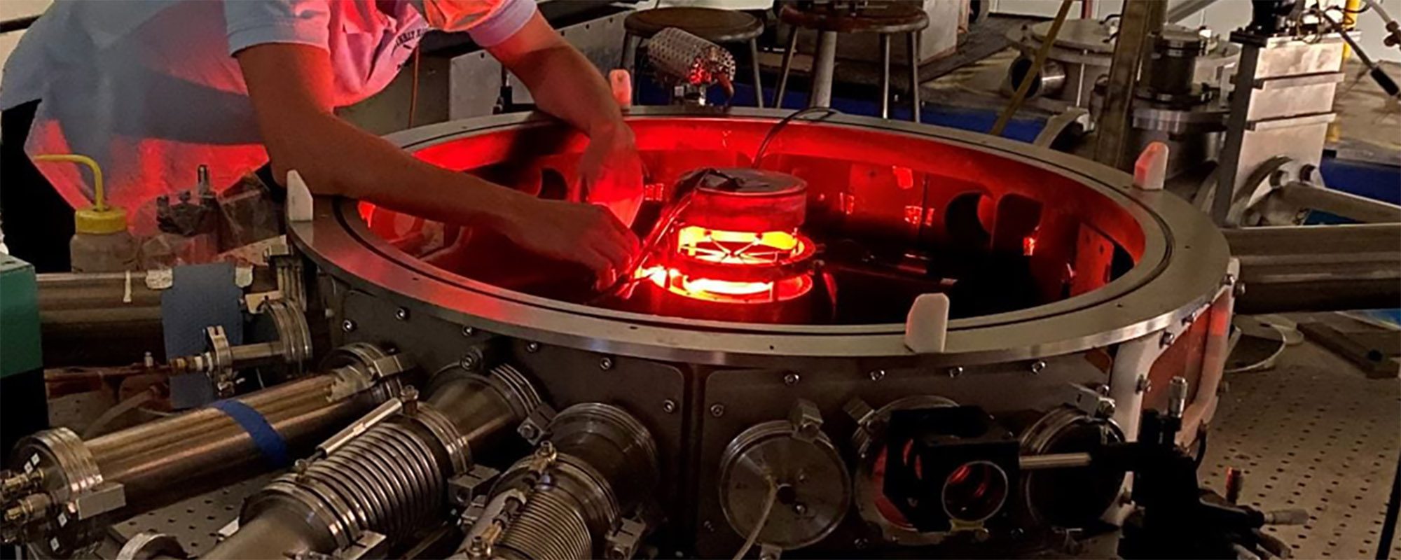 Man bends over a piece of circular equipment that glows red from center.