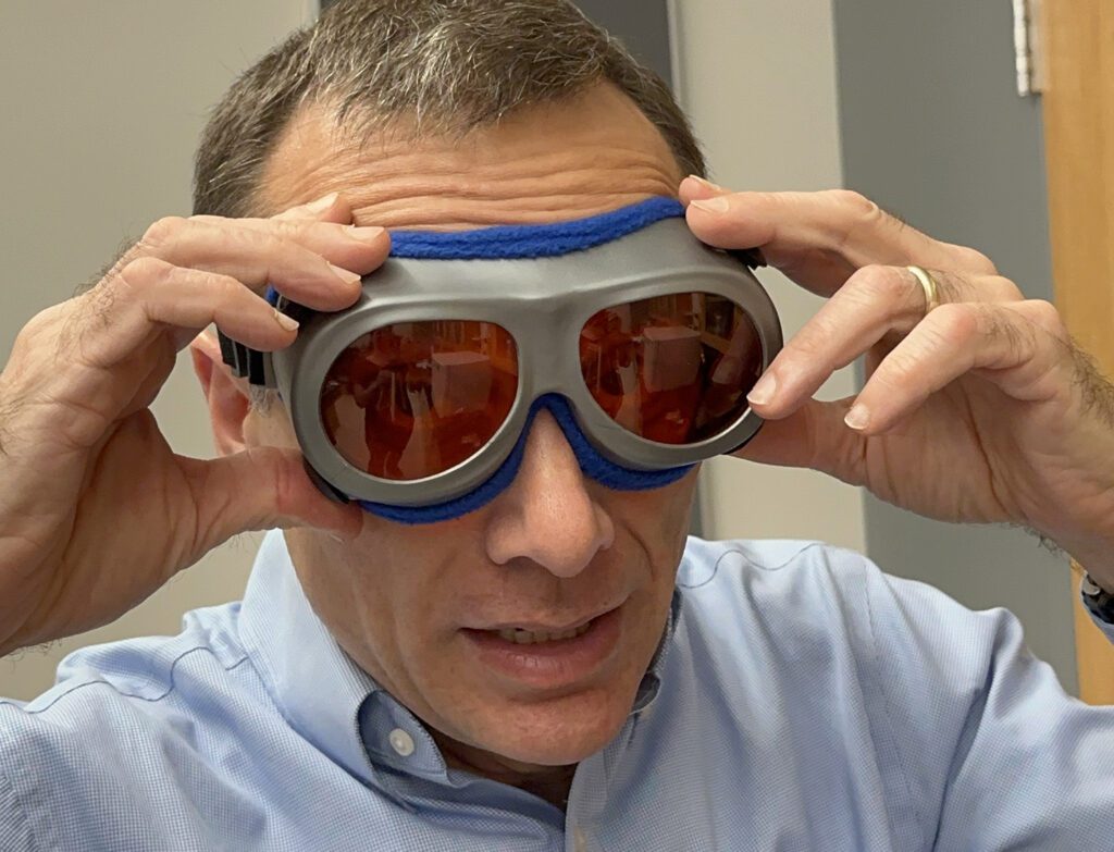 close-up of a man's face wearing tinted goggles. His hands are raised as if he has just put them on.