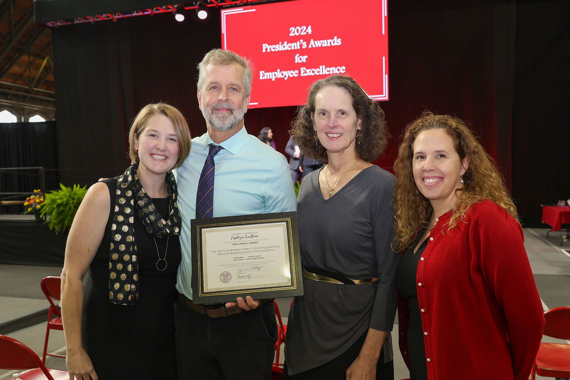 four people stand together and one is holding an award for the group.