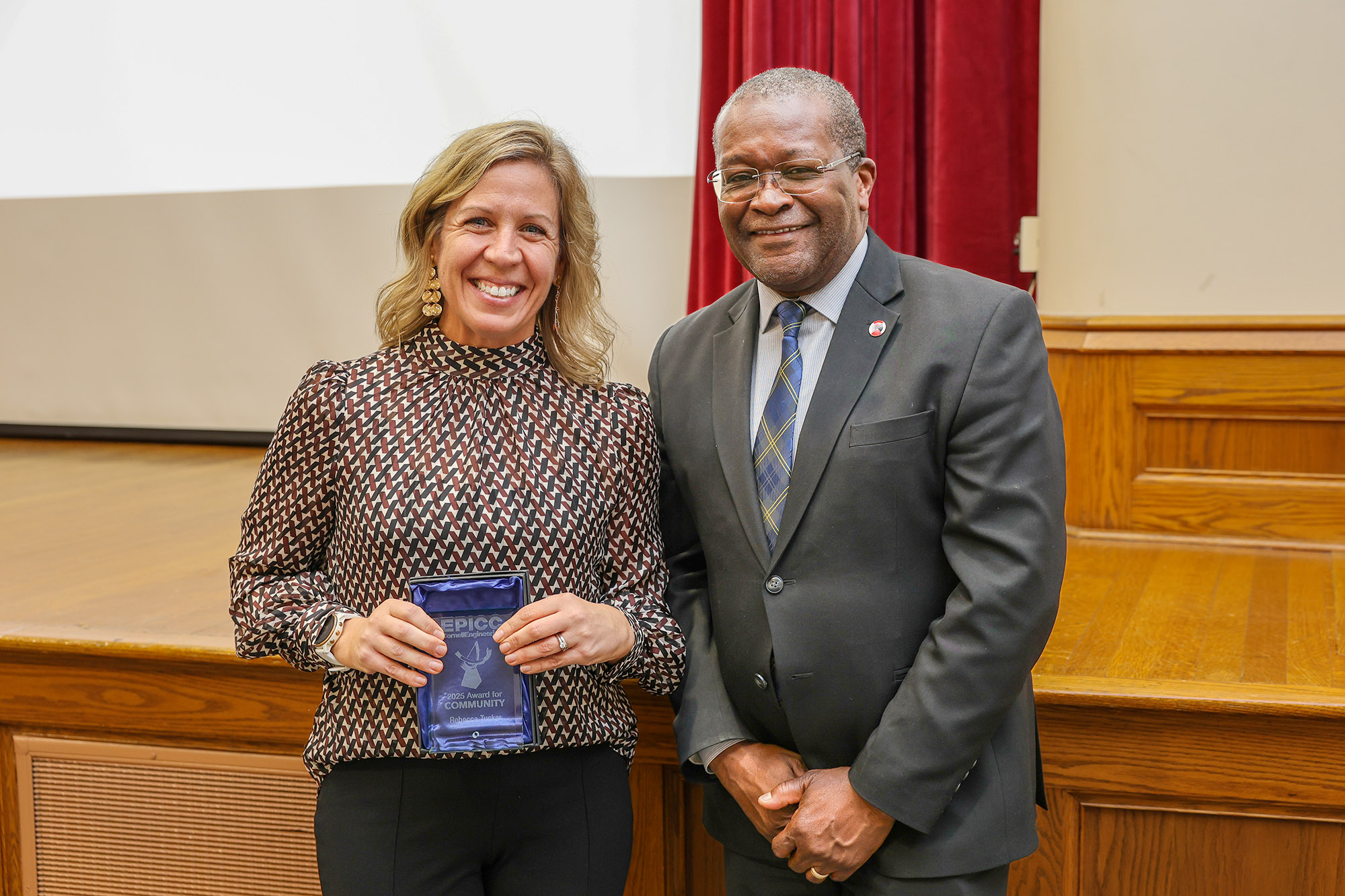 a woman and a man stand together, and the woman holds an award plaque.