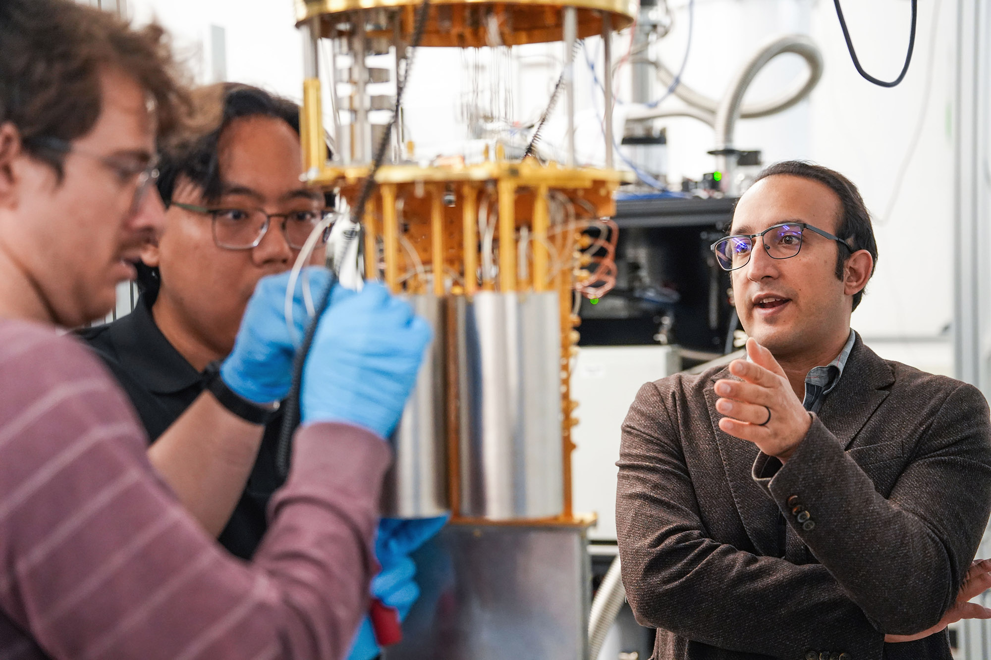 Two men work on a cryostat while another stands near.