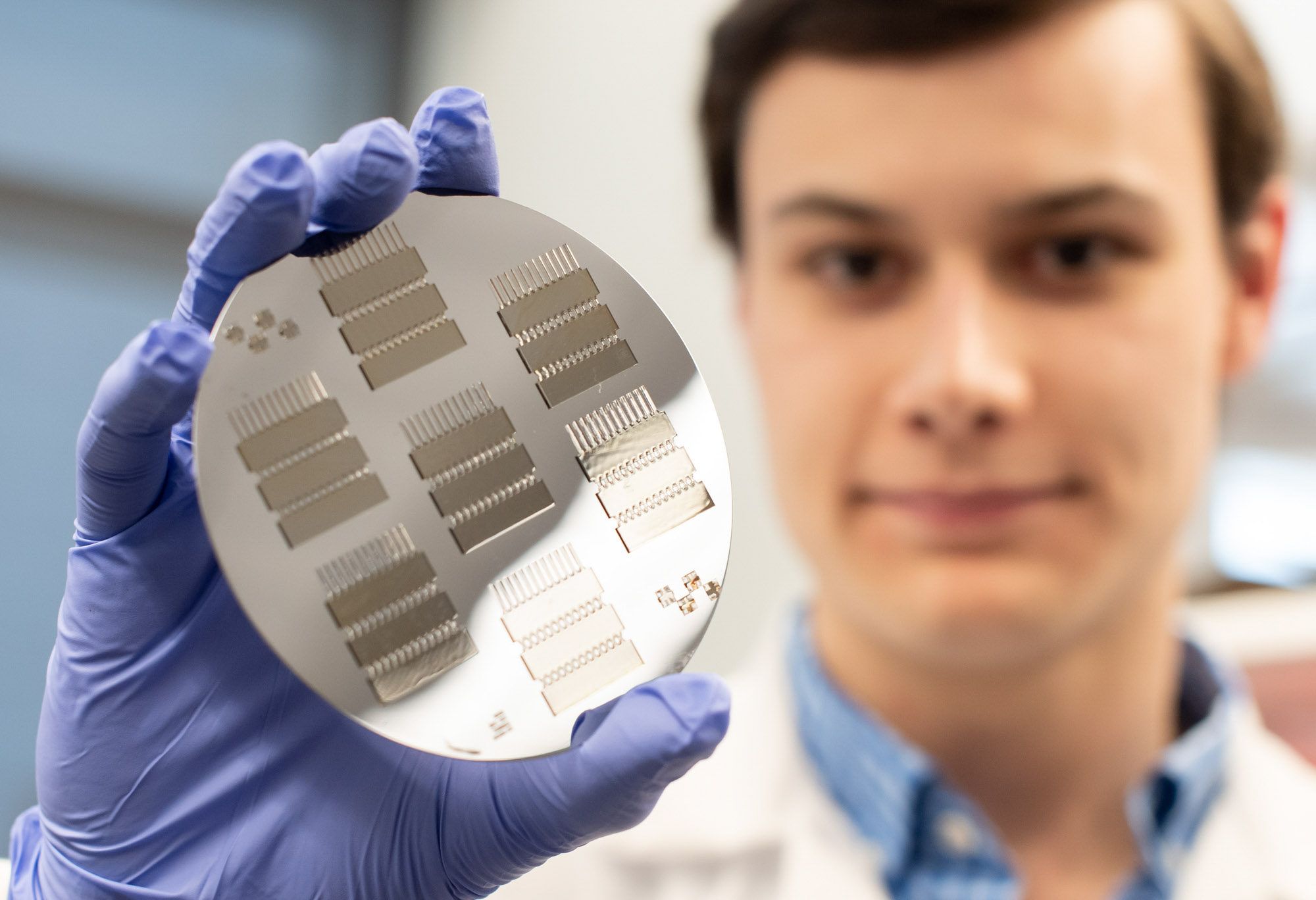 A researcher in the Esak Lee lab wearing a white lab coat and purple gloves holding a device.