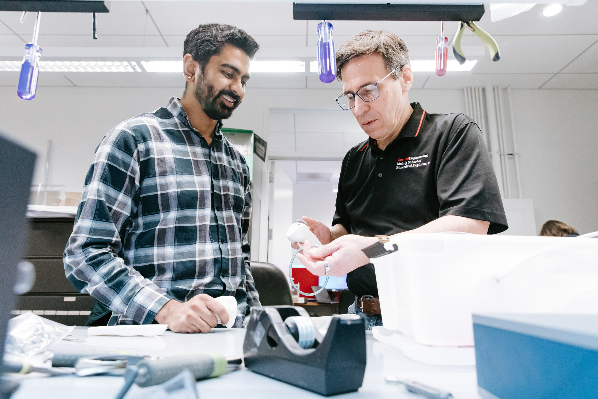Professor Newton DeFaria examines a prototype as a student smiles in one of the BME project teams spaces.