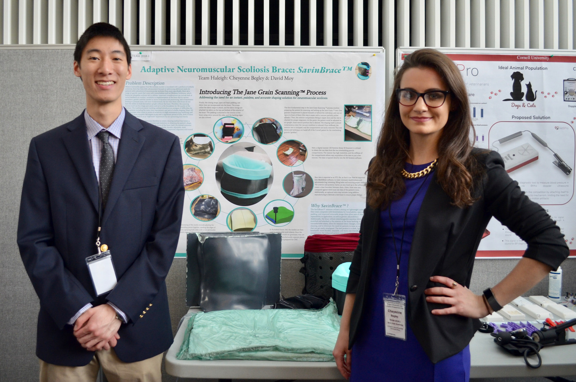Two students stand in front of their project and poster during the BME Industry Day M.Eng. Showcase.