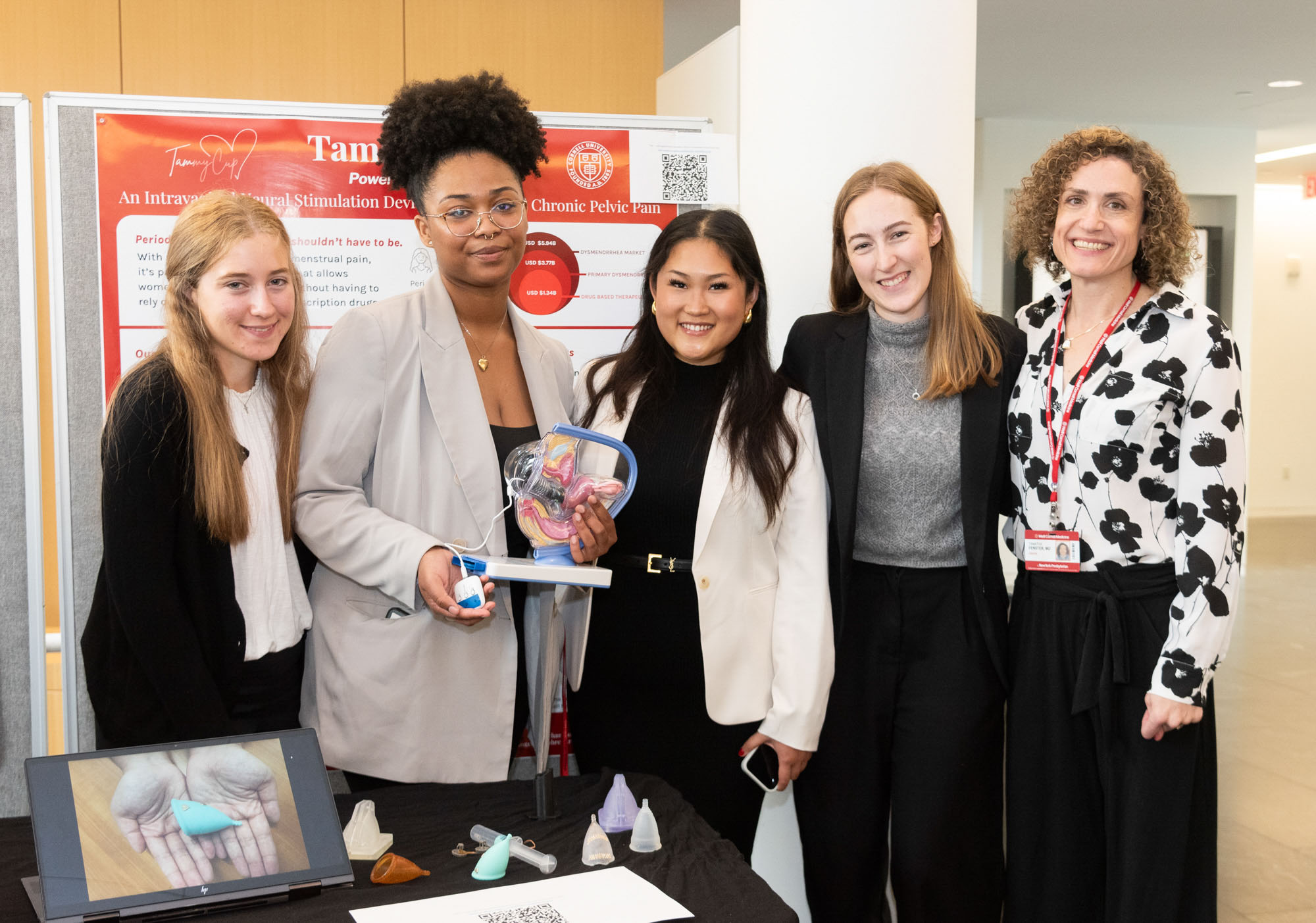 Five students in business attire stand at their booth at the BME Industry Day M.Eng. Showcase.