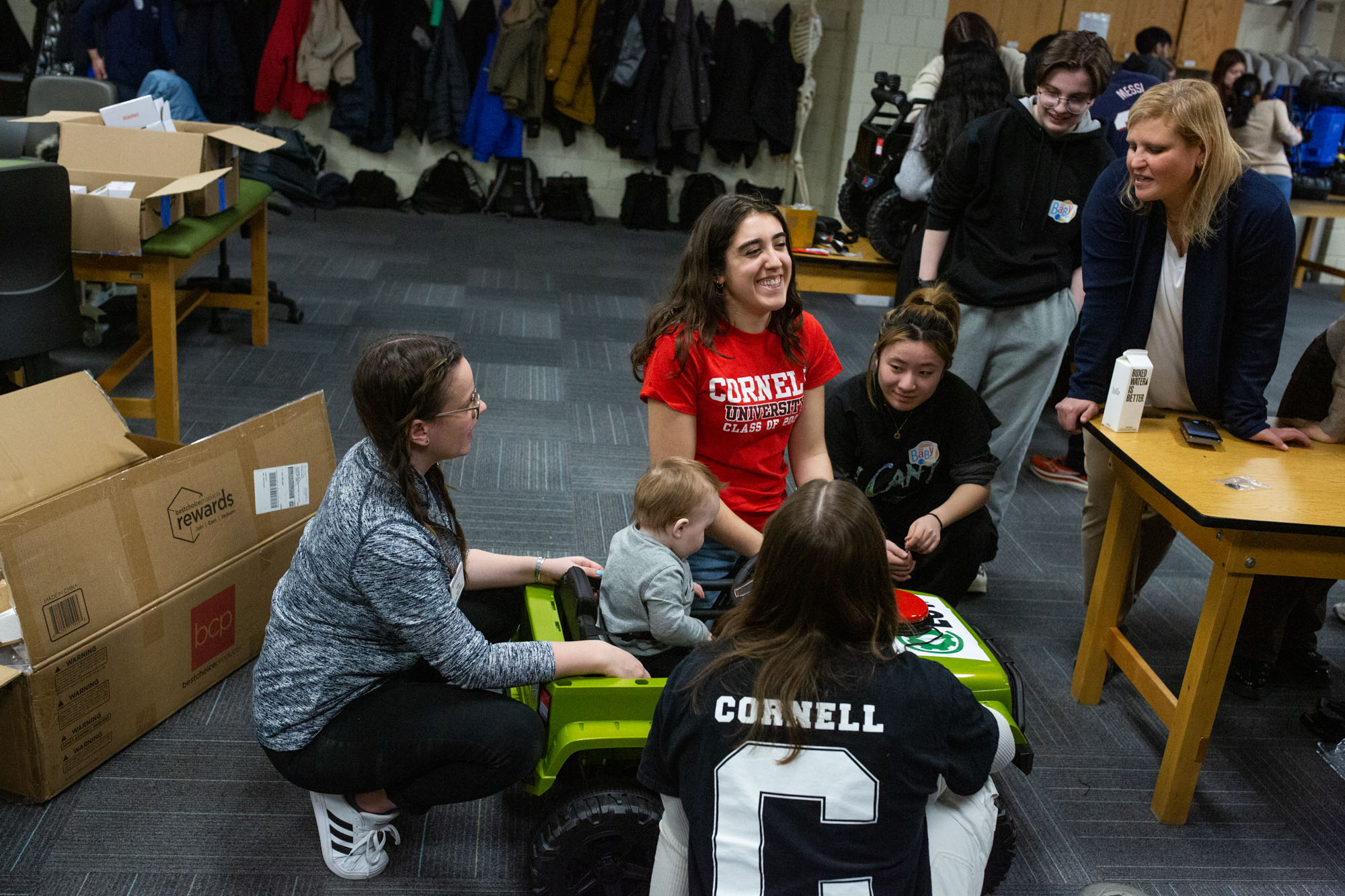 students sit around toy car with child sitting inside as part of Adaptive Play design and build event at Ithaca College