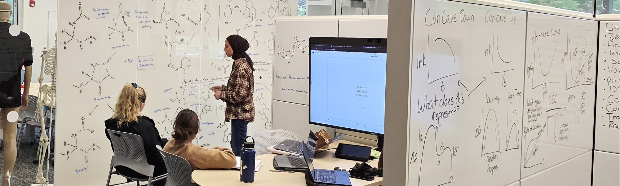Students discuss and draw chemical formulas on the design studio room walls in Tang Hall.