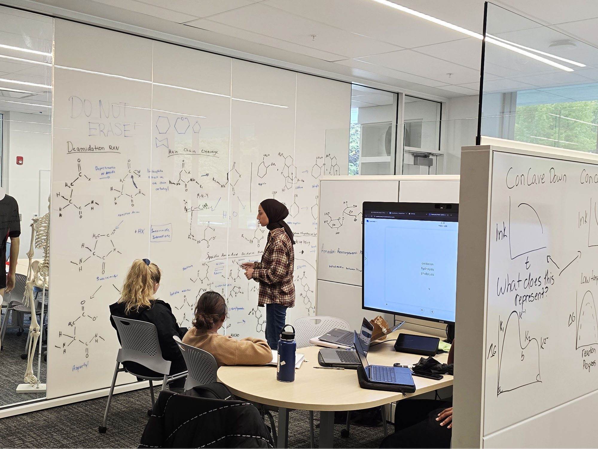 Students discuss and draw chemical formulas on the design studio room walls in Tang Hall.