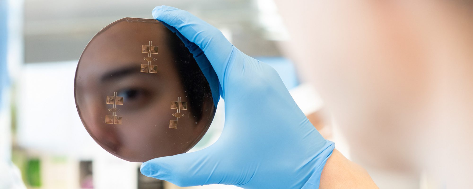 A person's face is reflected in a wafer held by somone wearing medical gloves.