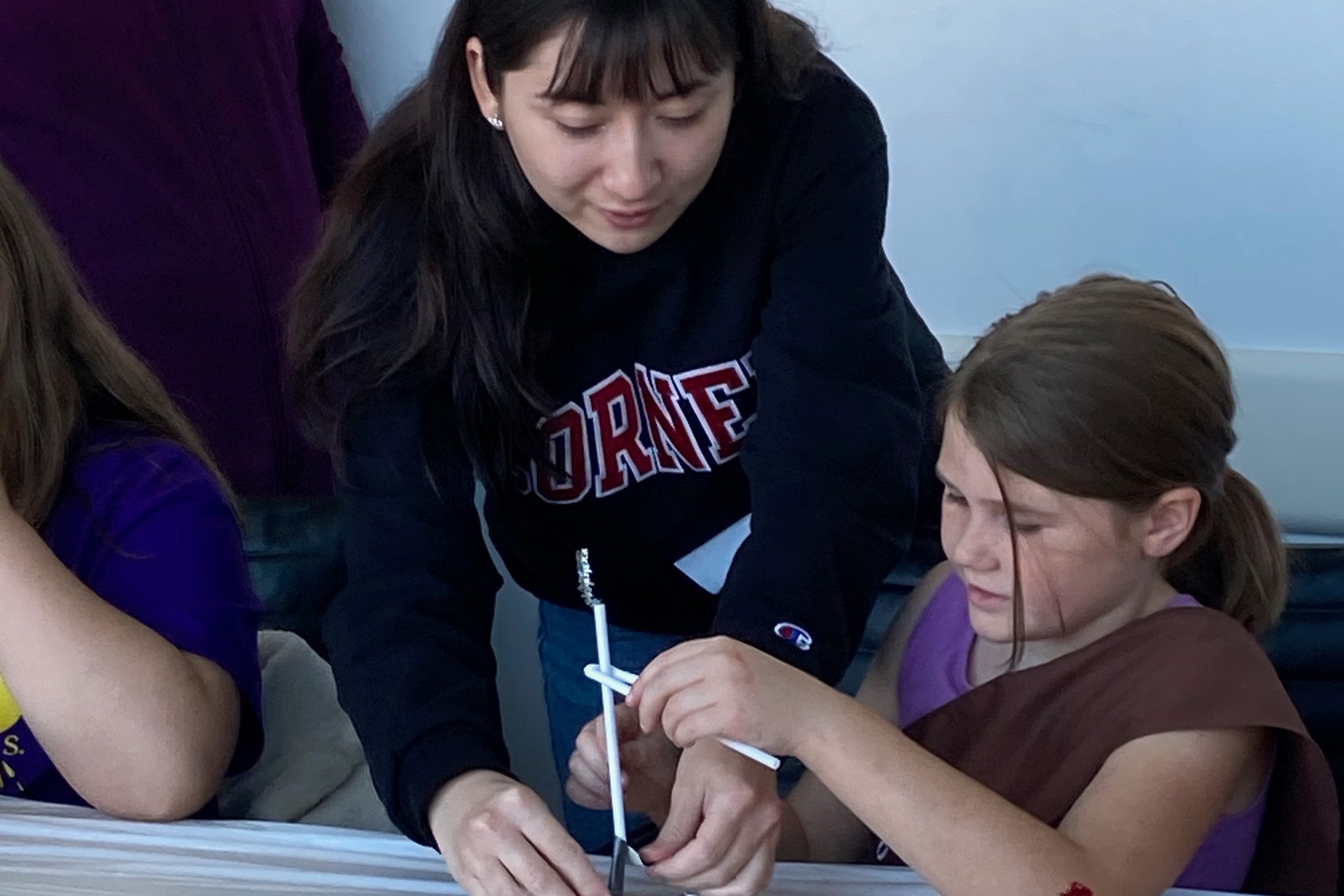 Cornell graduate student works with girl scout at table on an engineering experiment at GSED 2024.