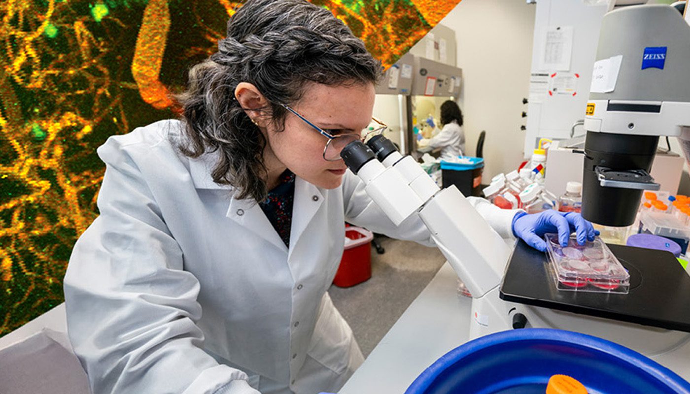 Postdoc in lab coat looks into microscope with test tube in ice.