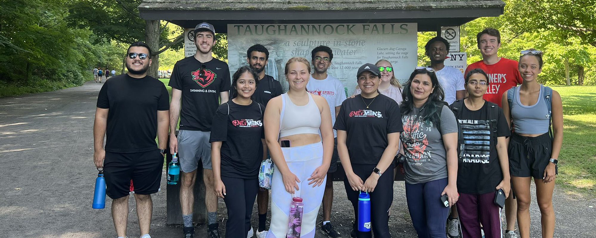 Graduate students standing together outside by Taughannock Falls hike sign.