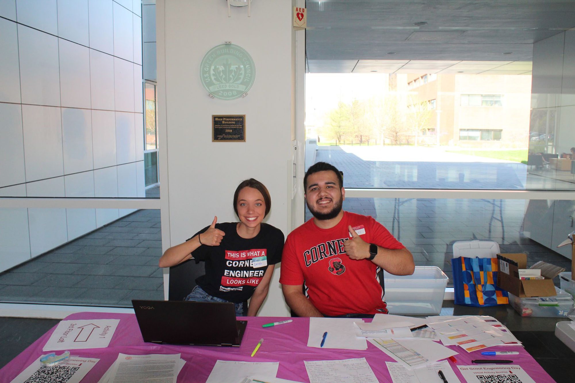 Graduate students sit at table in Weill Hall thumbs up for outreach event.