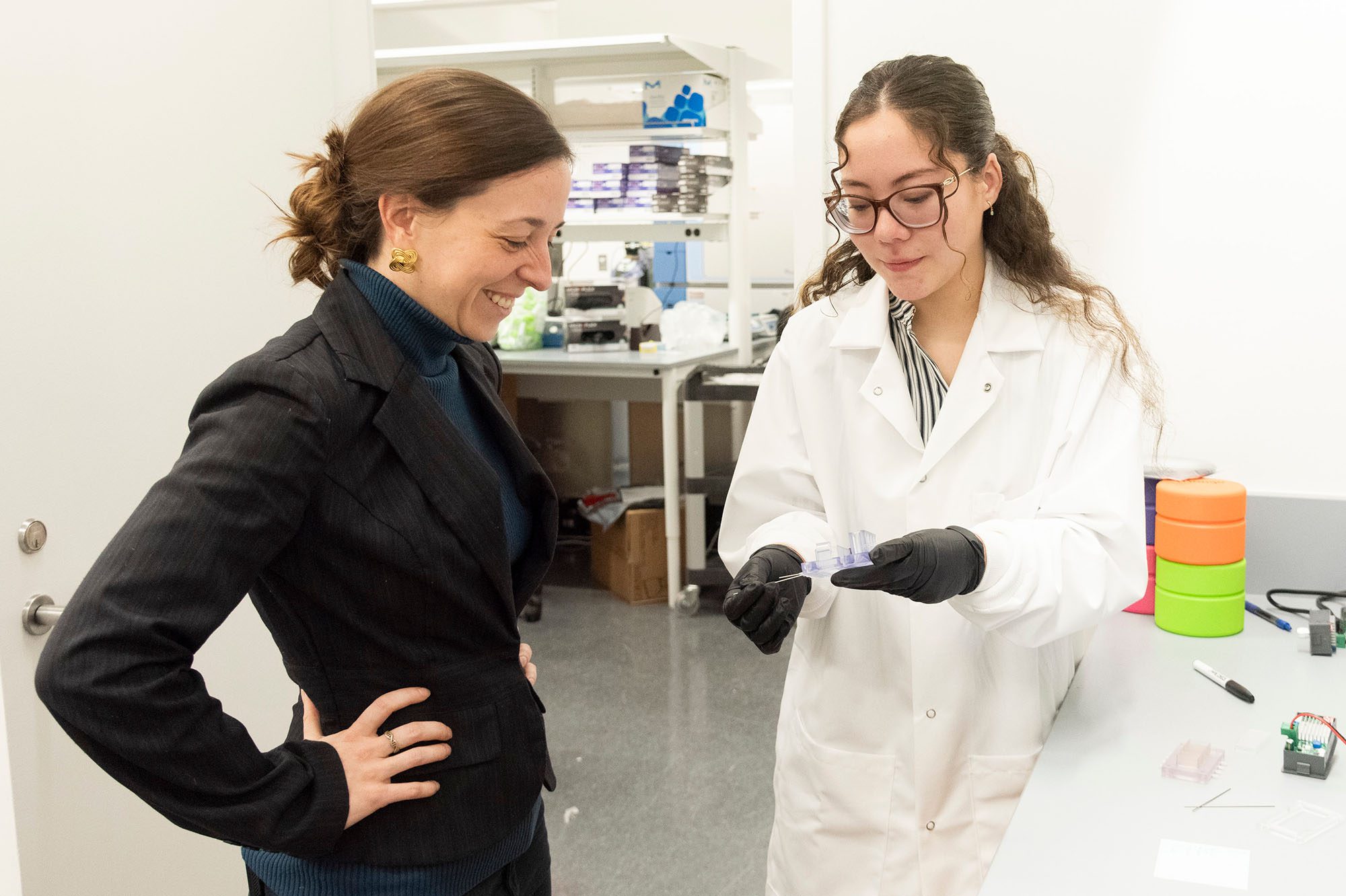 Kayla Wolf stands with student holding a device in a lab.