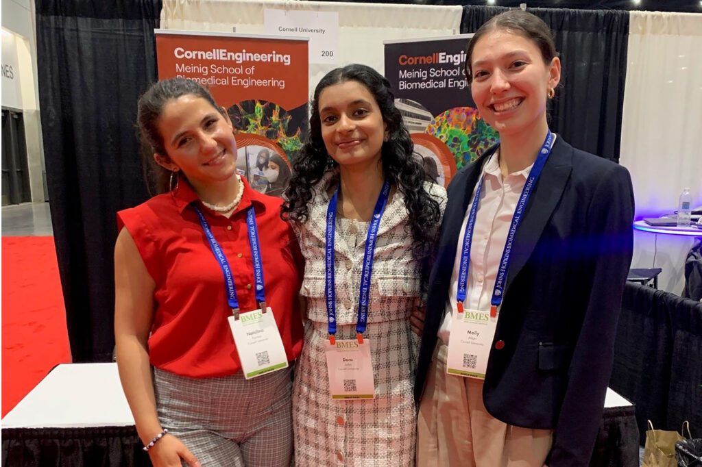 Three undergraduate students representatives of winning debut team stand together at BMES 2025 conference booth.