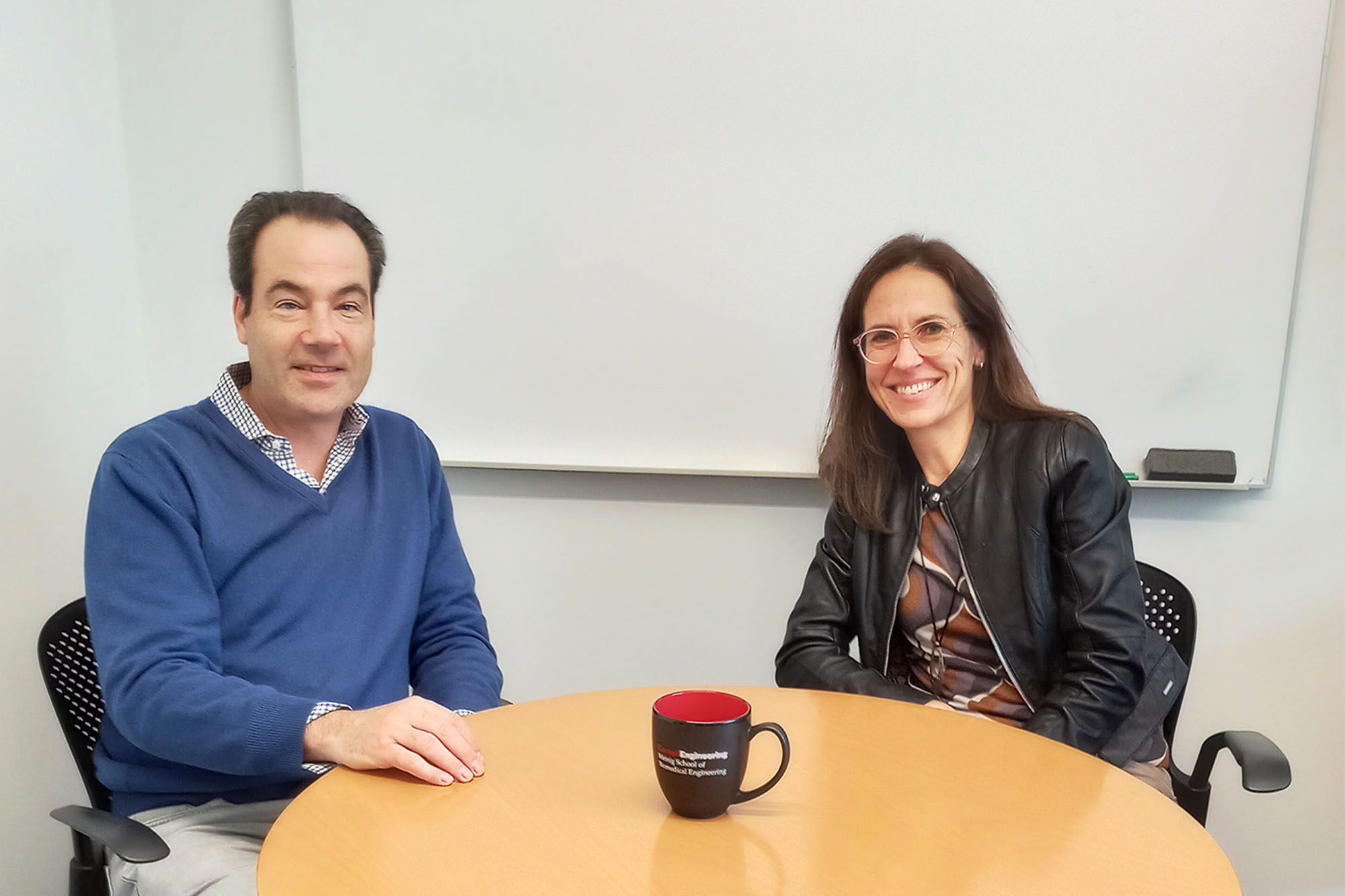 Jason Spector sits at a table with Claudia Fischbach in Weill Hall office.