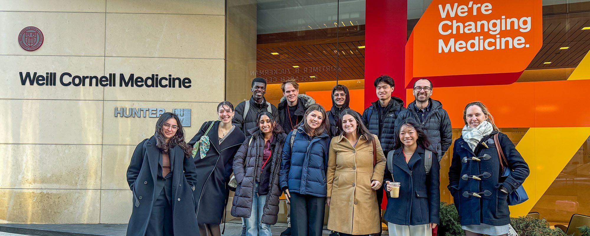Undergraduate clinical immersion students stand with faculty outside Weill Cornell Medicine sign in New York City.