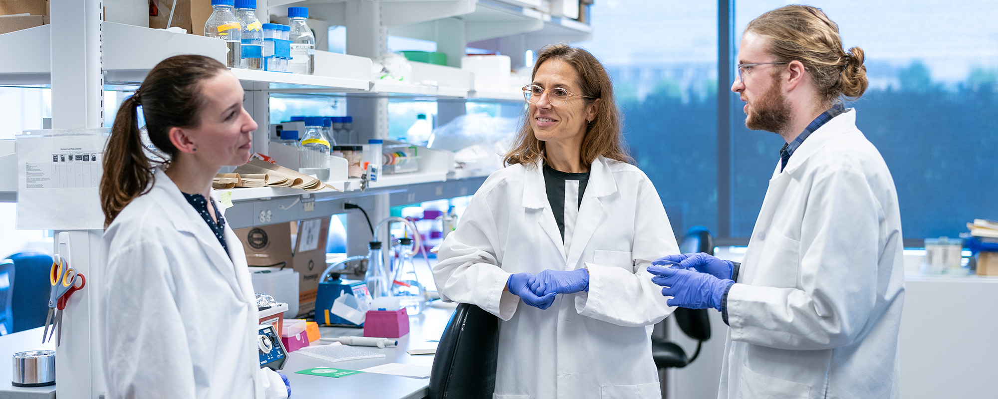 Claudia Fischbach and students wearing lab coats and talking.