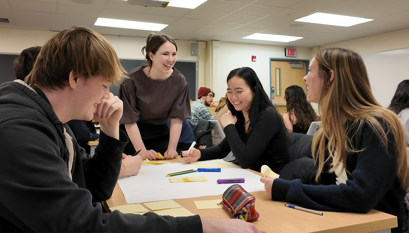Alex Werth speaks with undergraduate students at a table engineering education classroom.