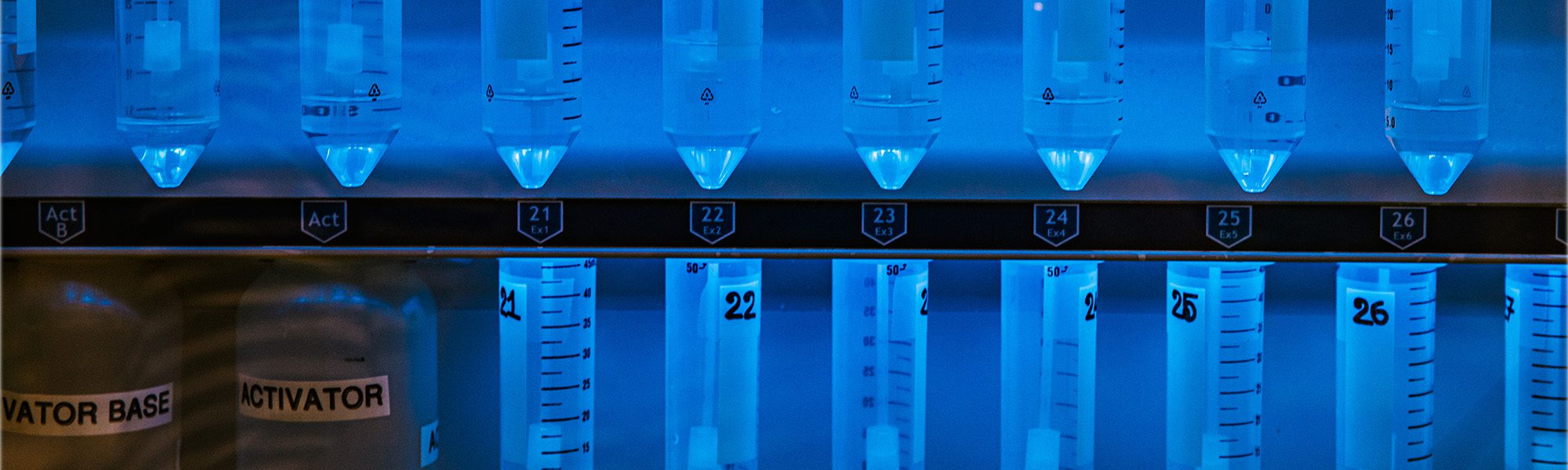 A line of illuminated liquid-filled tubes for biomolecular testing lined up in a fume hood.