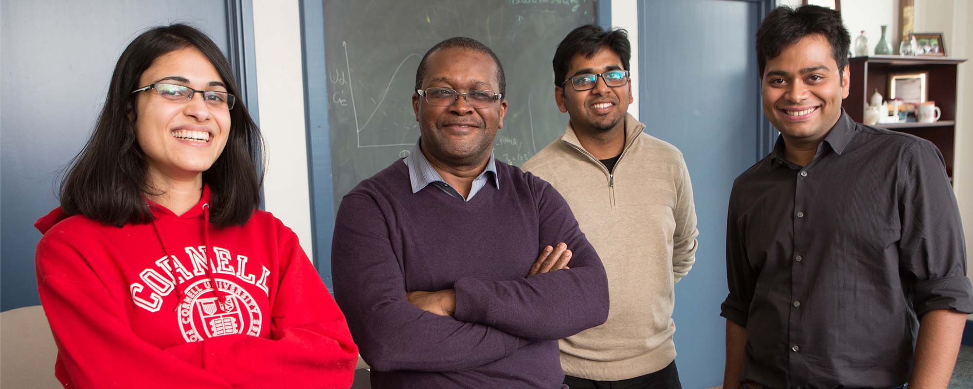 Dean Lynden Archer is standing in front of a chalk board in his office with three graduate students.