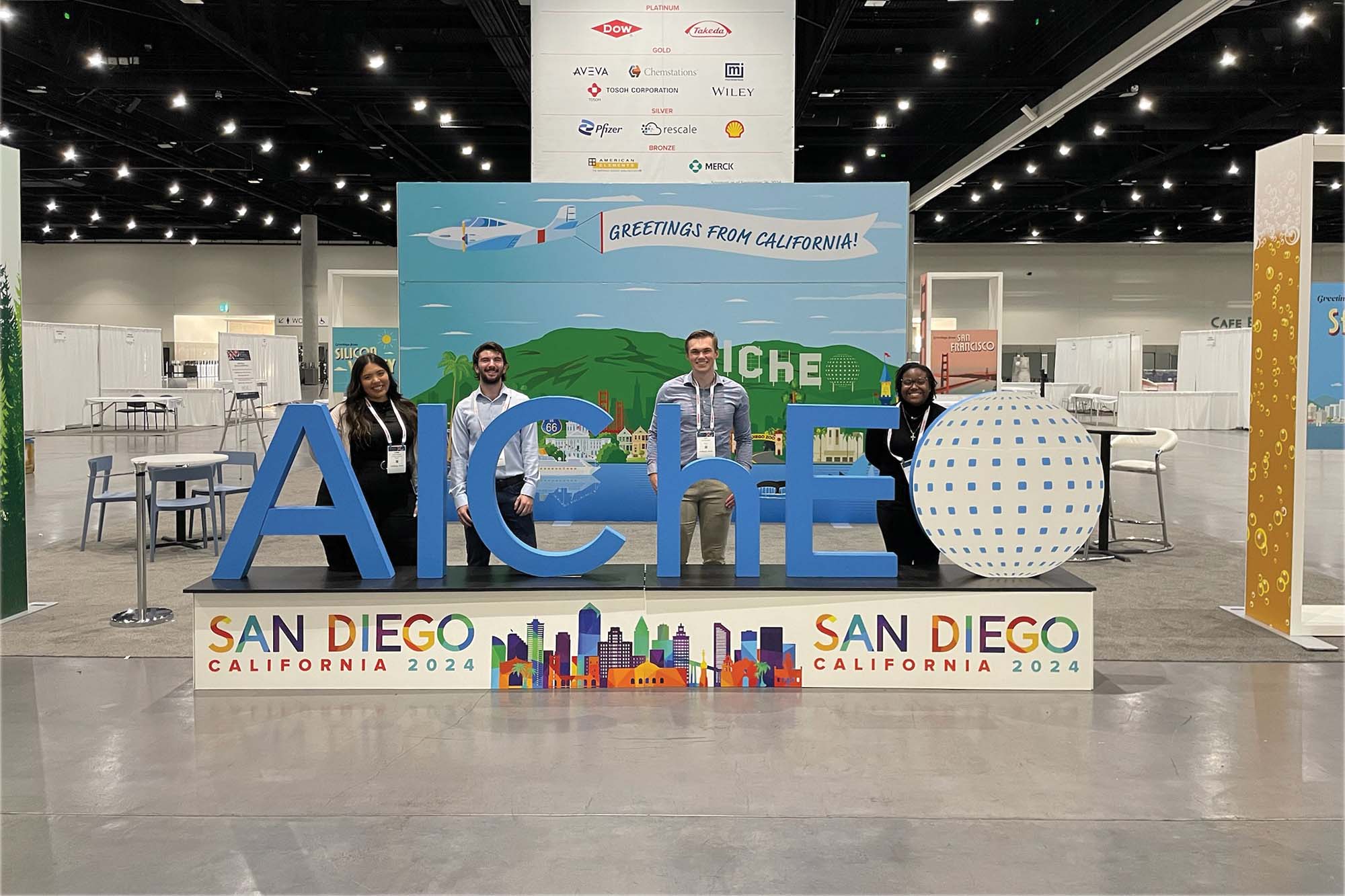 Graduate students stand at the AICHE conference sign in San Diego California 2024.