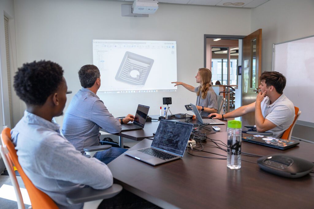 MEng student team members chat with Rev assistant director Deanna Kocher about developing their design.