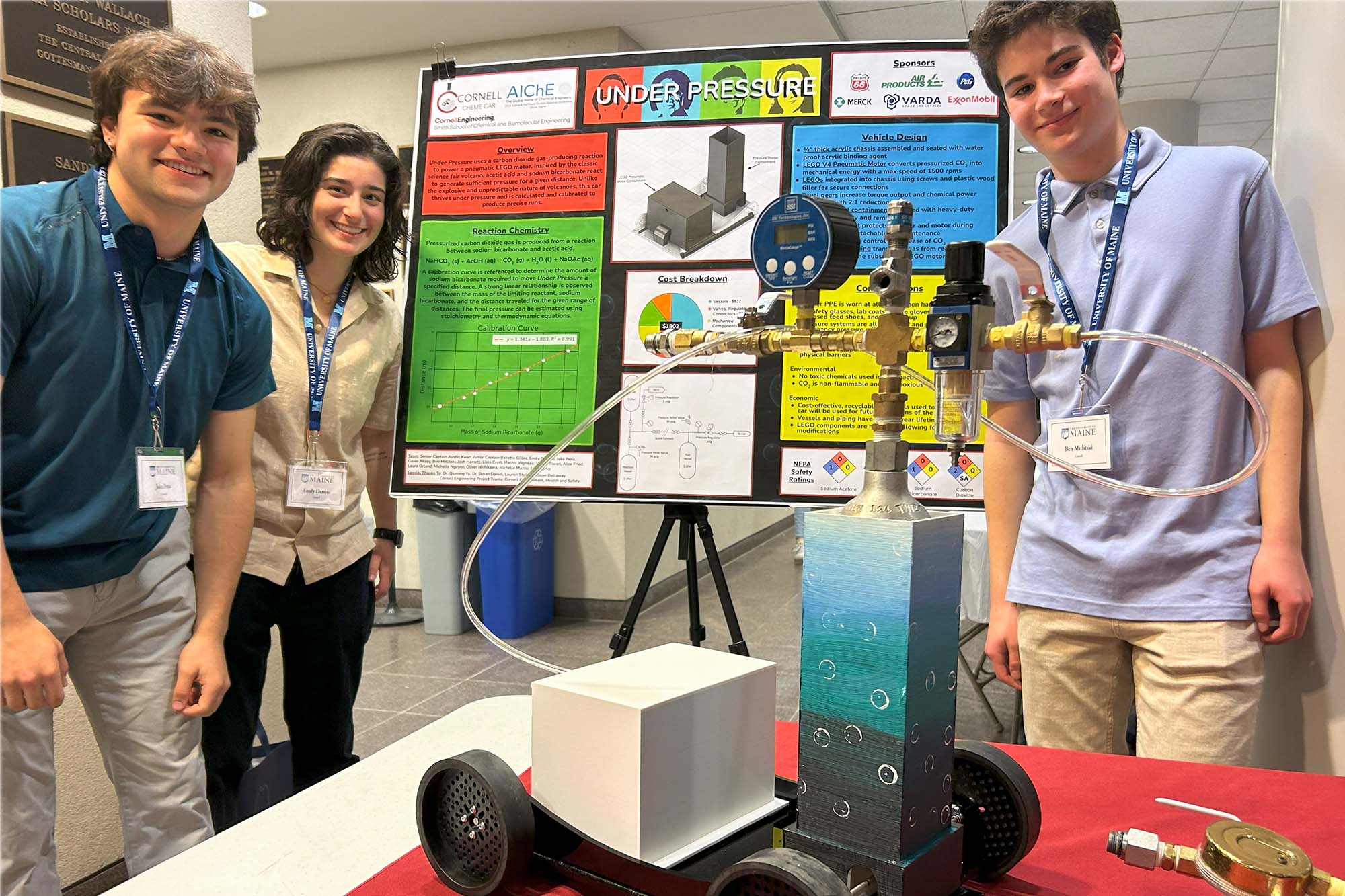 Undergraduate students stand with ChemE car and winning poster titled 