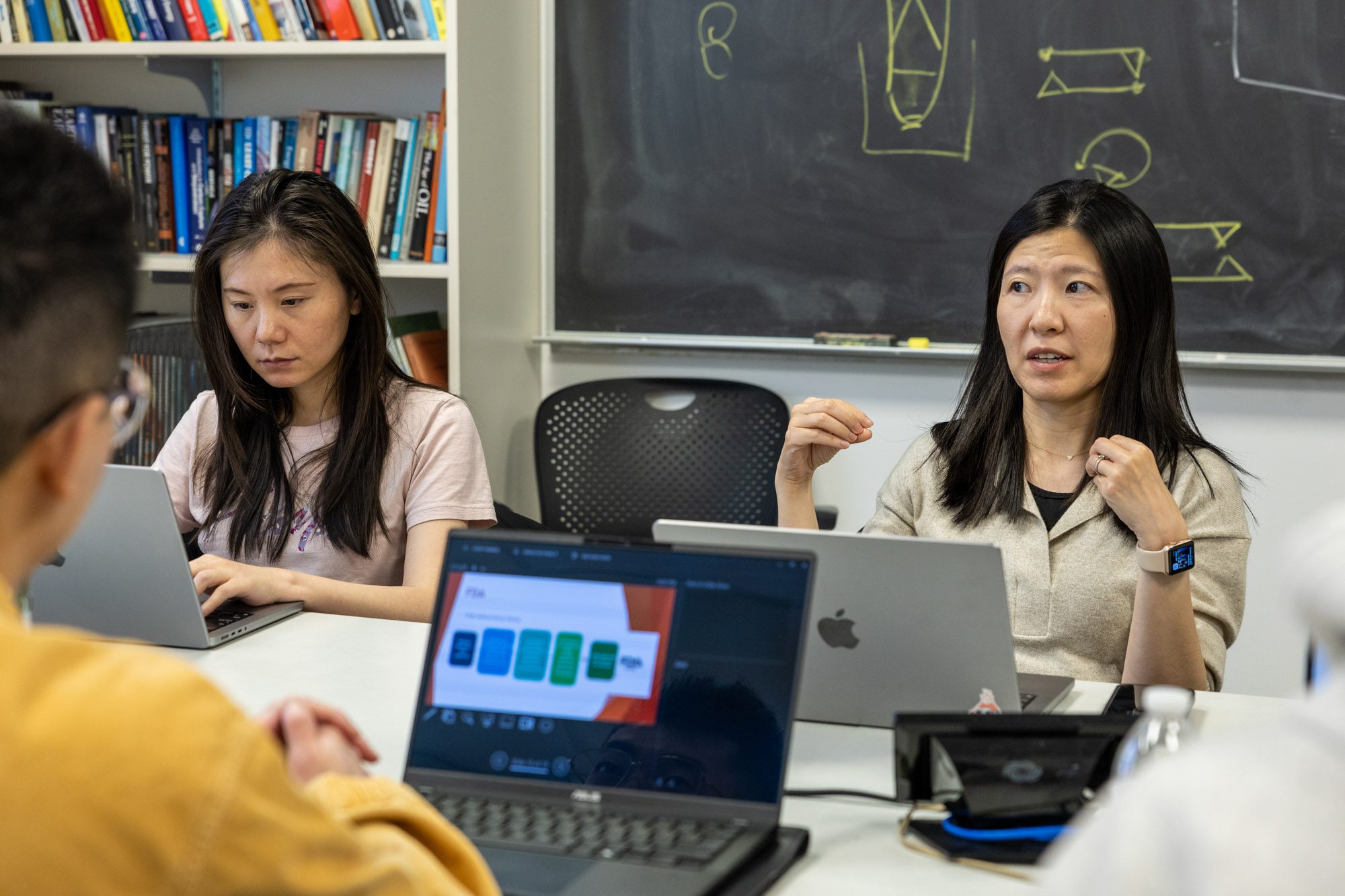 M.Eng. Students and professor Rong Yang work at table with laptops on their project 