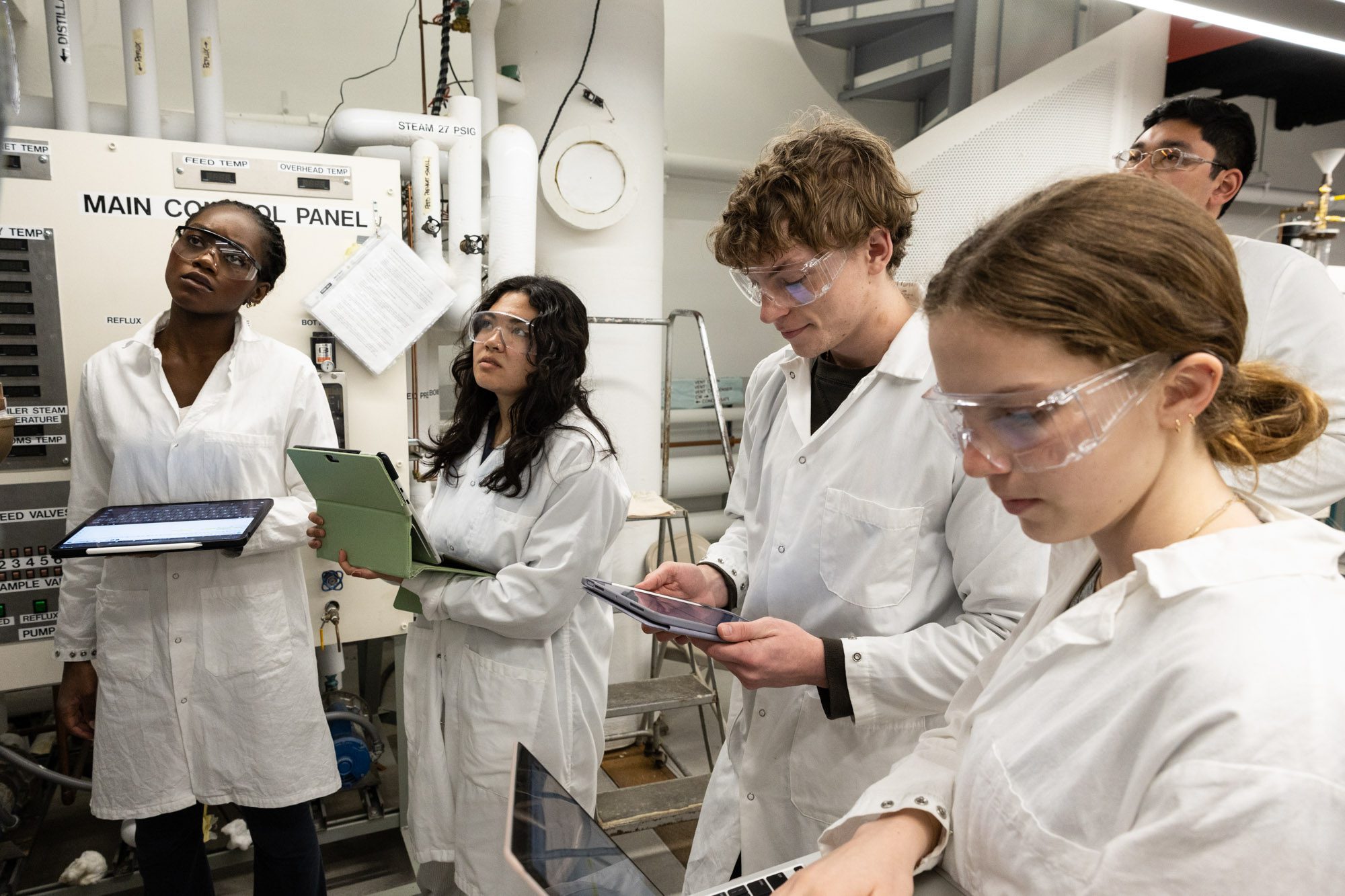 Undergraduate students wearing lab coats work with computers in the Olin Hall Unit Operations Lab.