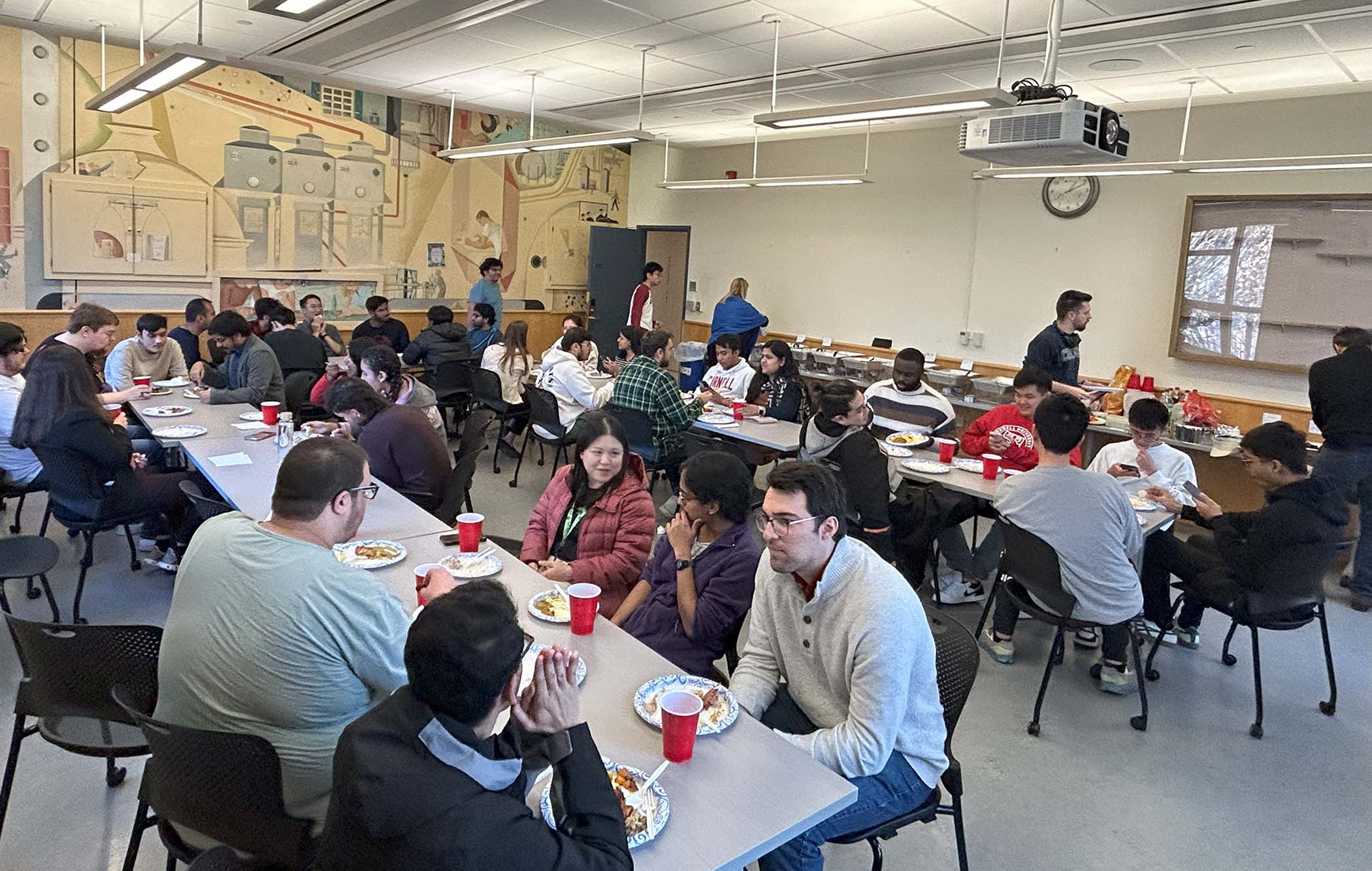 Graduate students sit together at tables enjoying a potluck dinner and networking with each other.