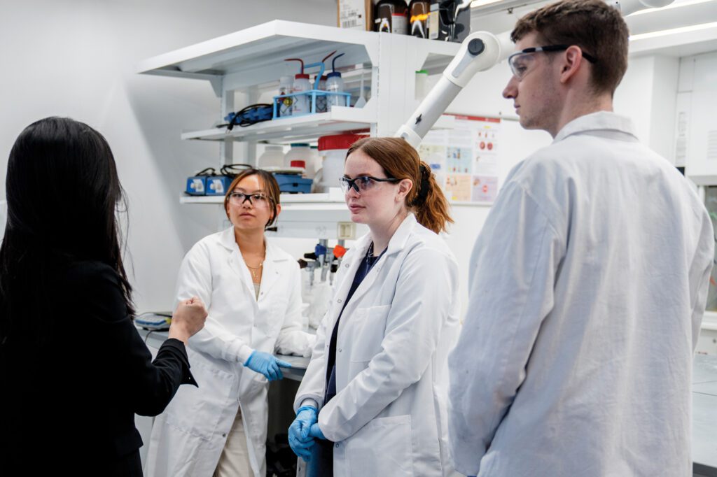 Julia Salatti (center) stands with peers wearing lab coats and professor Rong Yang in the ChemE 6400 lab in Olin Hall.