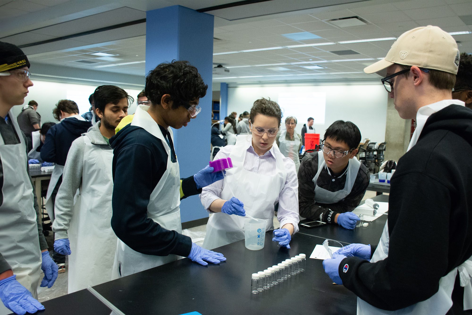Allison Godwin in lab coat working with undergraduate students in Olin Hall lab.