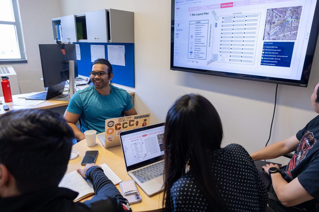 MEng students in team Tesla design project talk together at a table with laptops and screens in Brian Bauer's office.