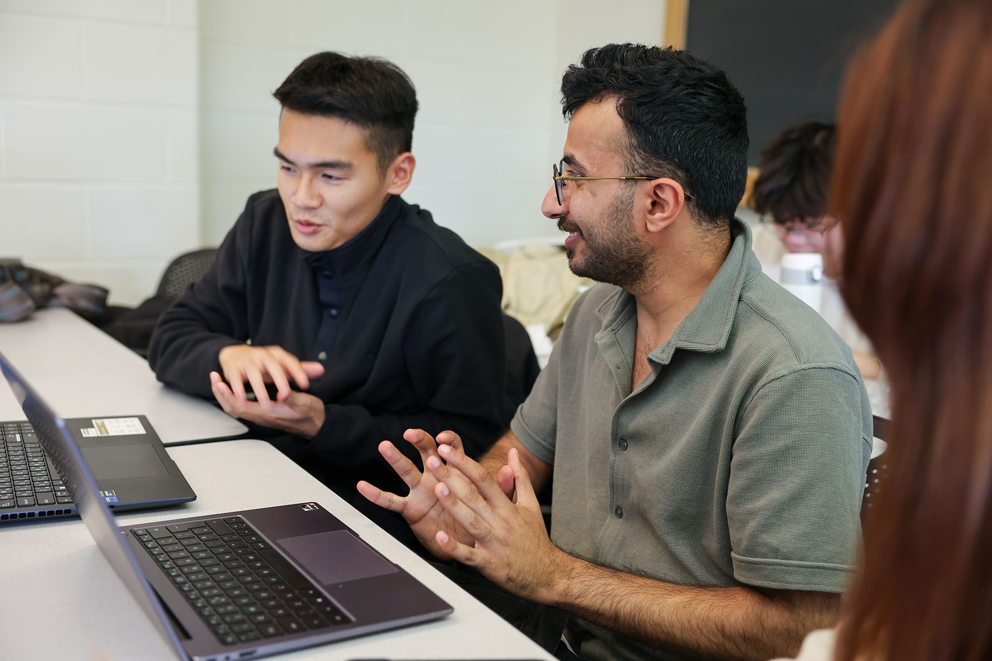 Two MEng students chat at a table with laptops.
