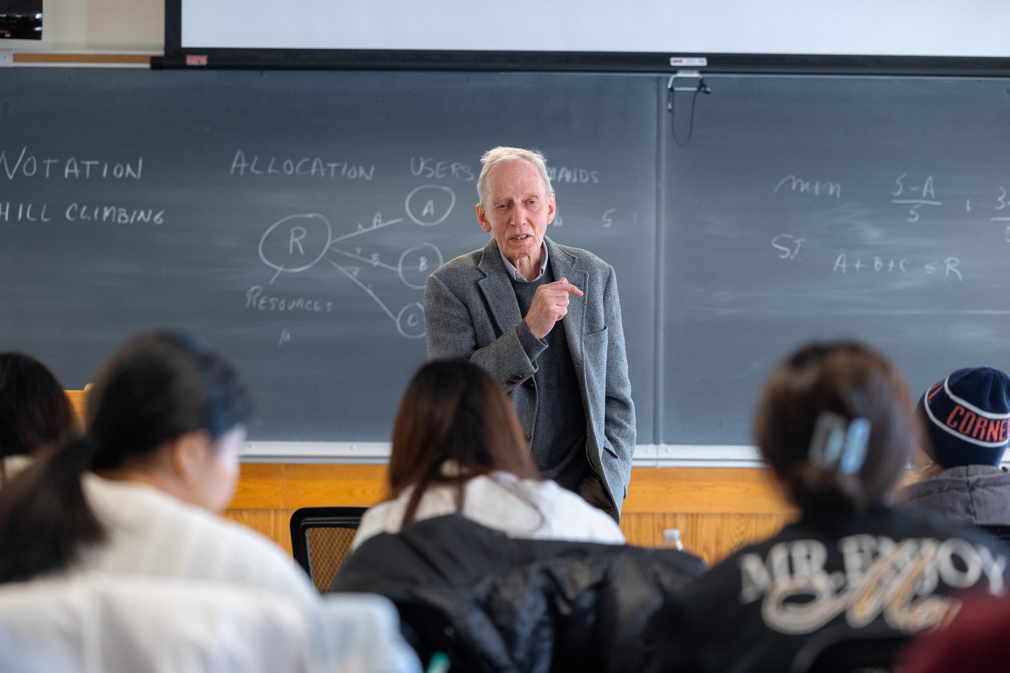Daniel Peter Loucks stands in front of a blackboard teaching a class