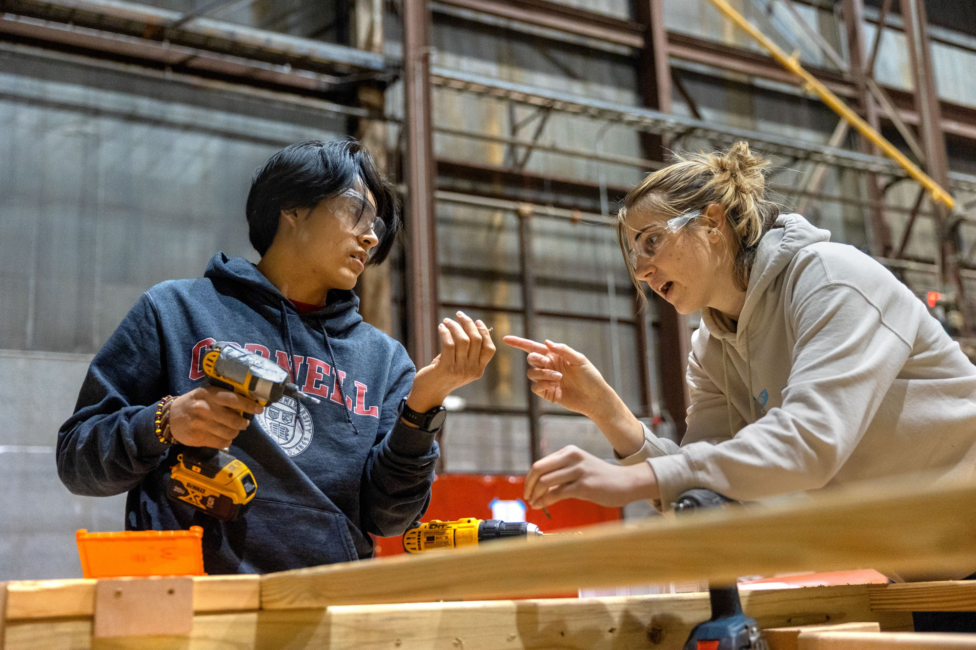 Two students using a power drill in the high voltage lab to connect wooden planks for the flat rock bridge project