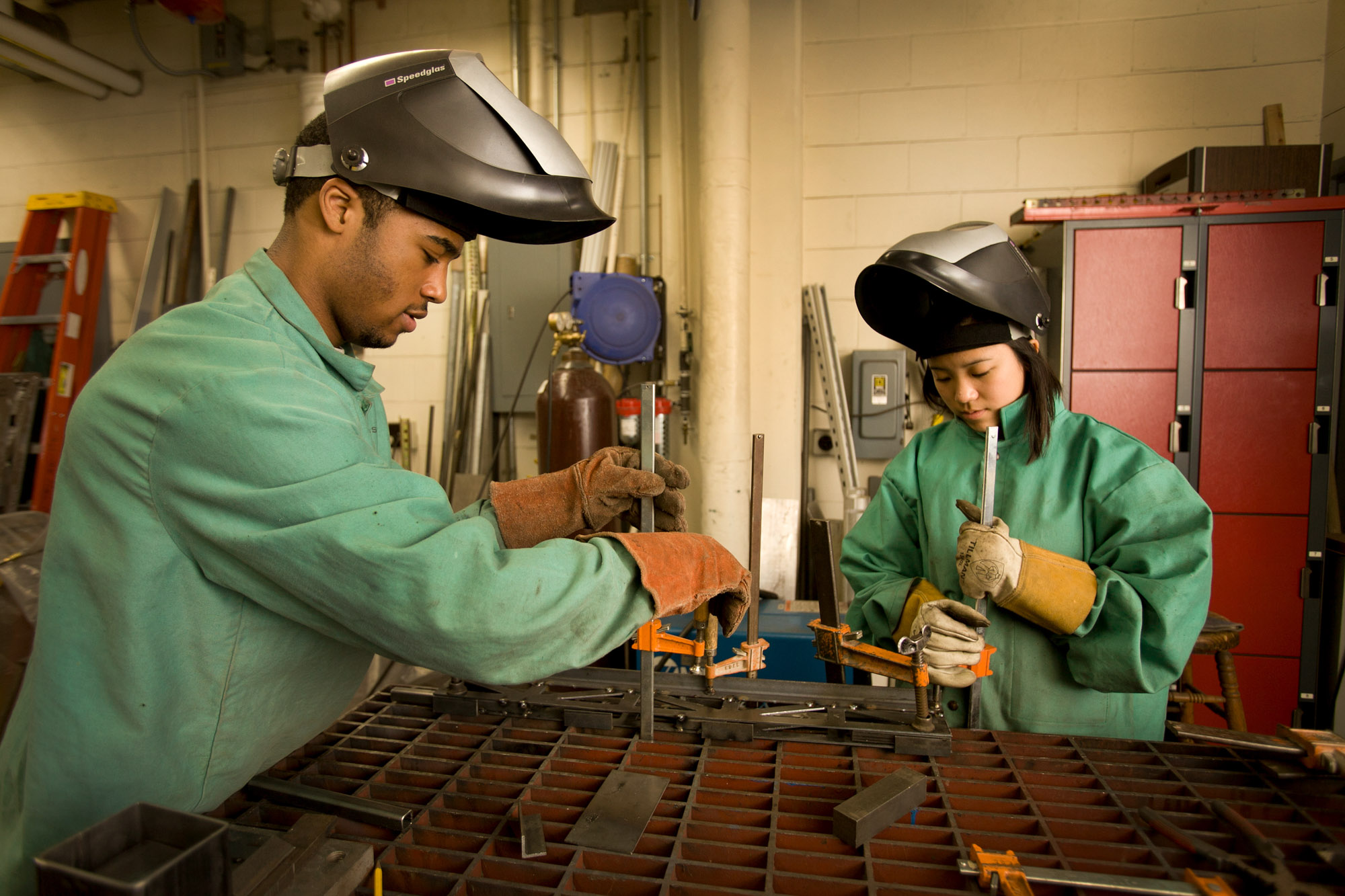 Two students wearing welding hoods working in a civil and environmental engineering lab