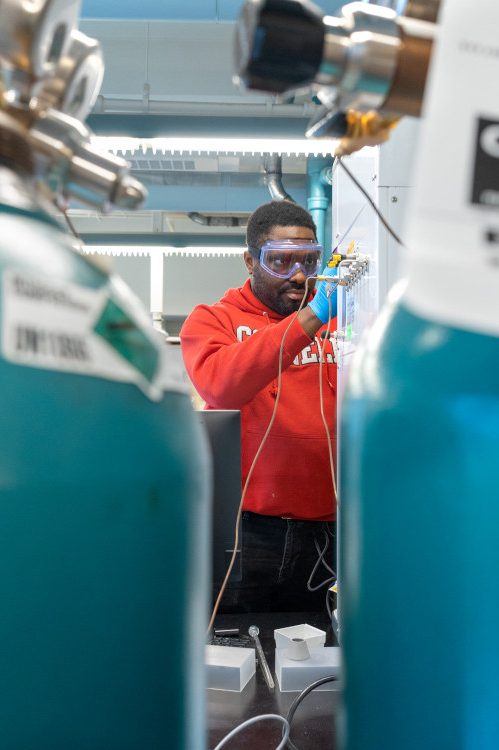 student wearing red sweatshirt working on lab equipment in-between two greenish blue tanks