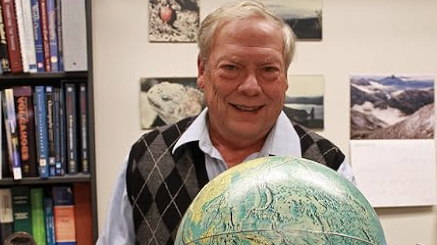 Bill White poses in his office with a globe in front of him.