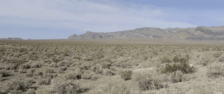 Desert scrubland in the foreground, dry mountains in the background with a partly