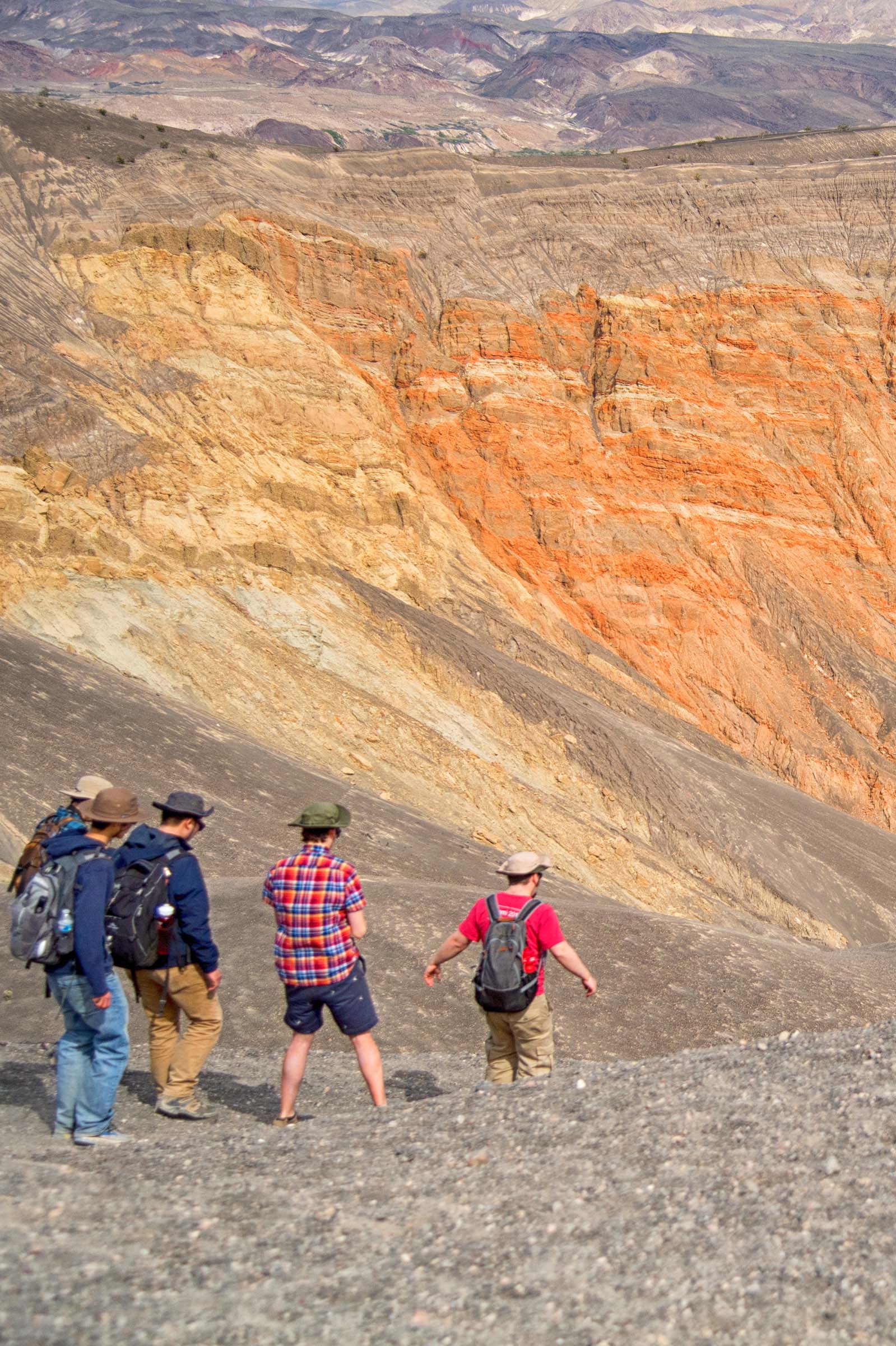 five people in casual hiking clothes descend into a rocky valley in a dry, treeless landscape.