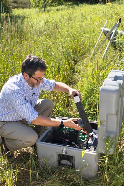 Geoff Abers unpacks seismographic equipment in a grassy field on a sunny day.
