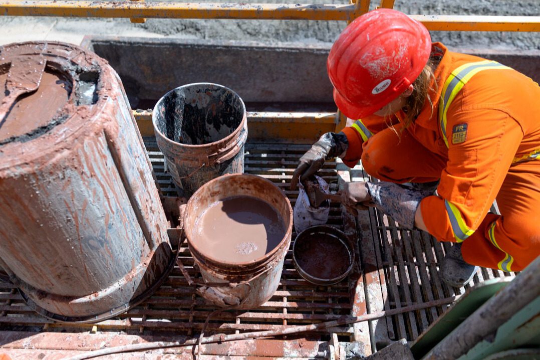 student in orange coveralls and a hard hat pulling rock samples from mud at the Cornell University Borehole Observatory.
