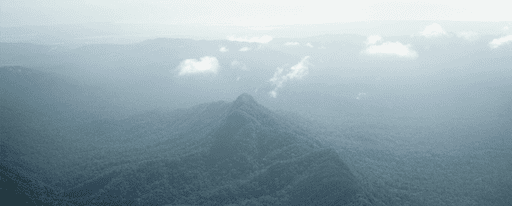 small white clouds and general haze over green forested mountains in Belize.