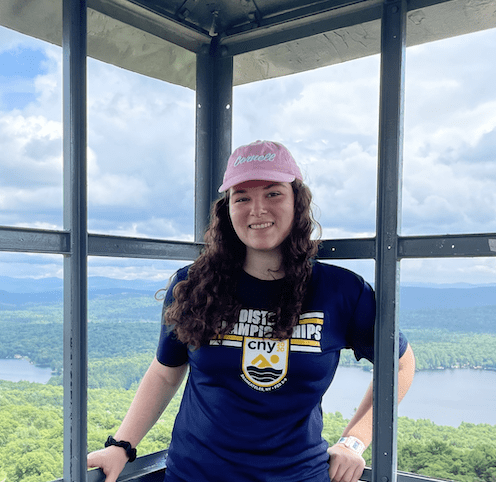 Rose Barris smiles in front of an elevated view of lakes and forrest.