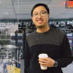 Jian Xun Wang holding a coffee cup standing in a lap