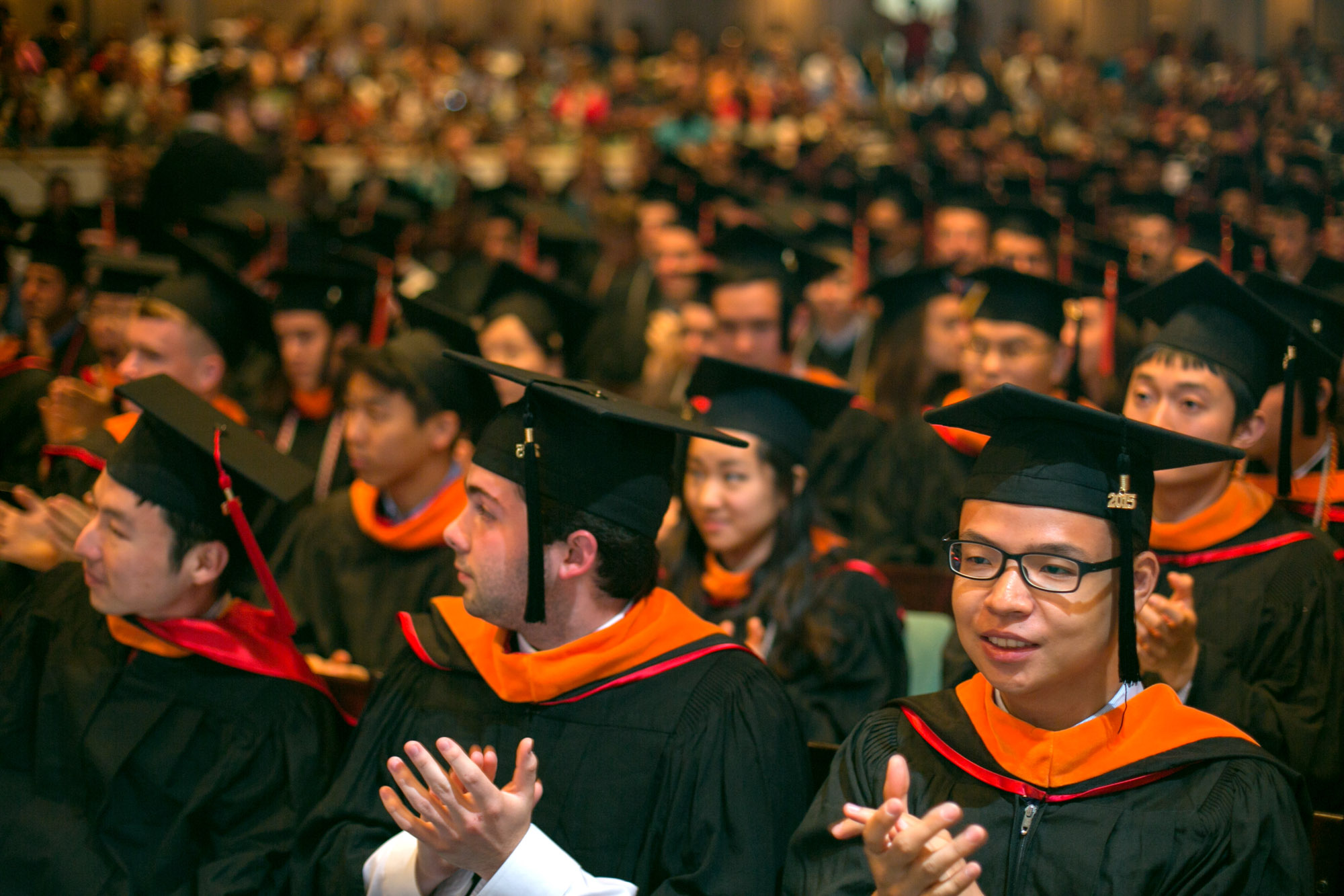 Graduating students in caps and gowns clap during ceremony in Bailey Hall.