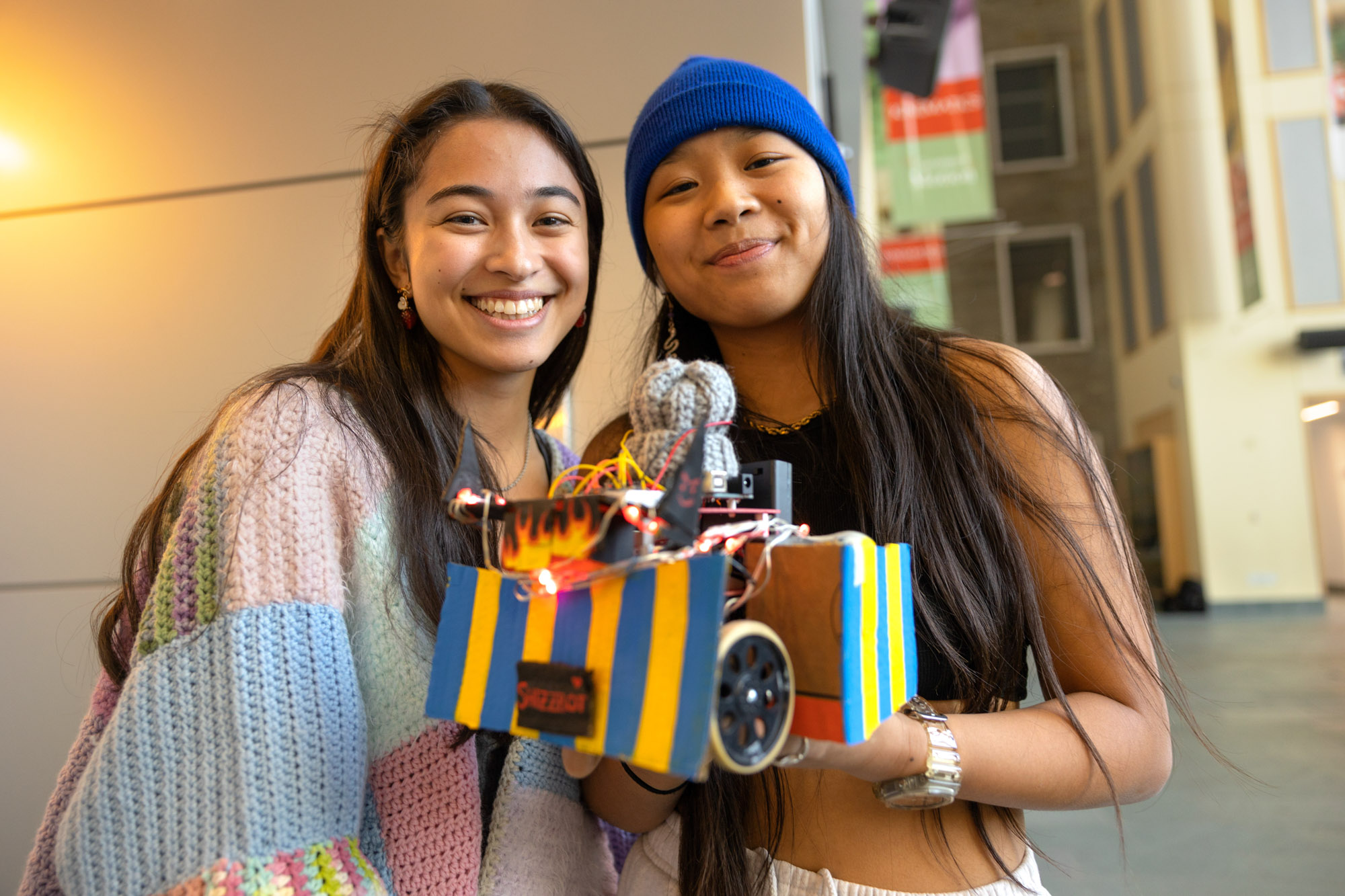 Two smiling students hold a robot.
