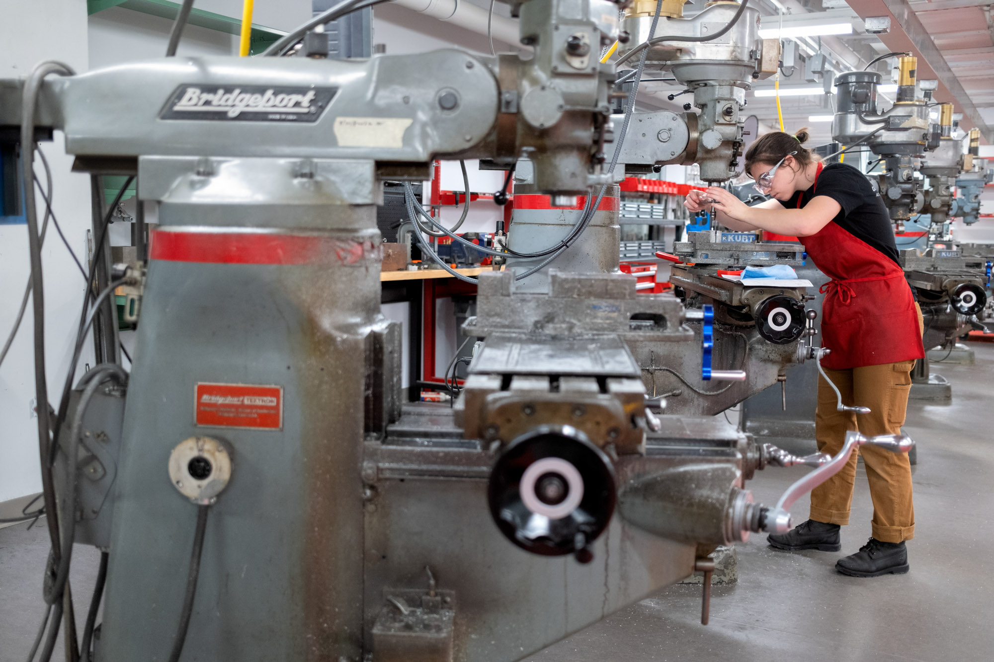 A female student operates a drill press in a machine shop.
